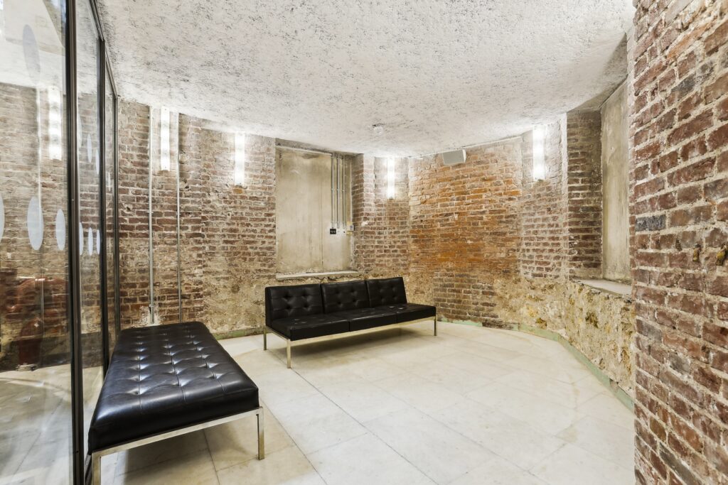 Brick-walled alcove with black seating benches and vertical wall lights, adjacent to a glass partition.