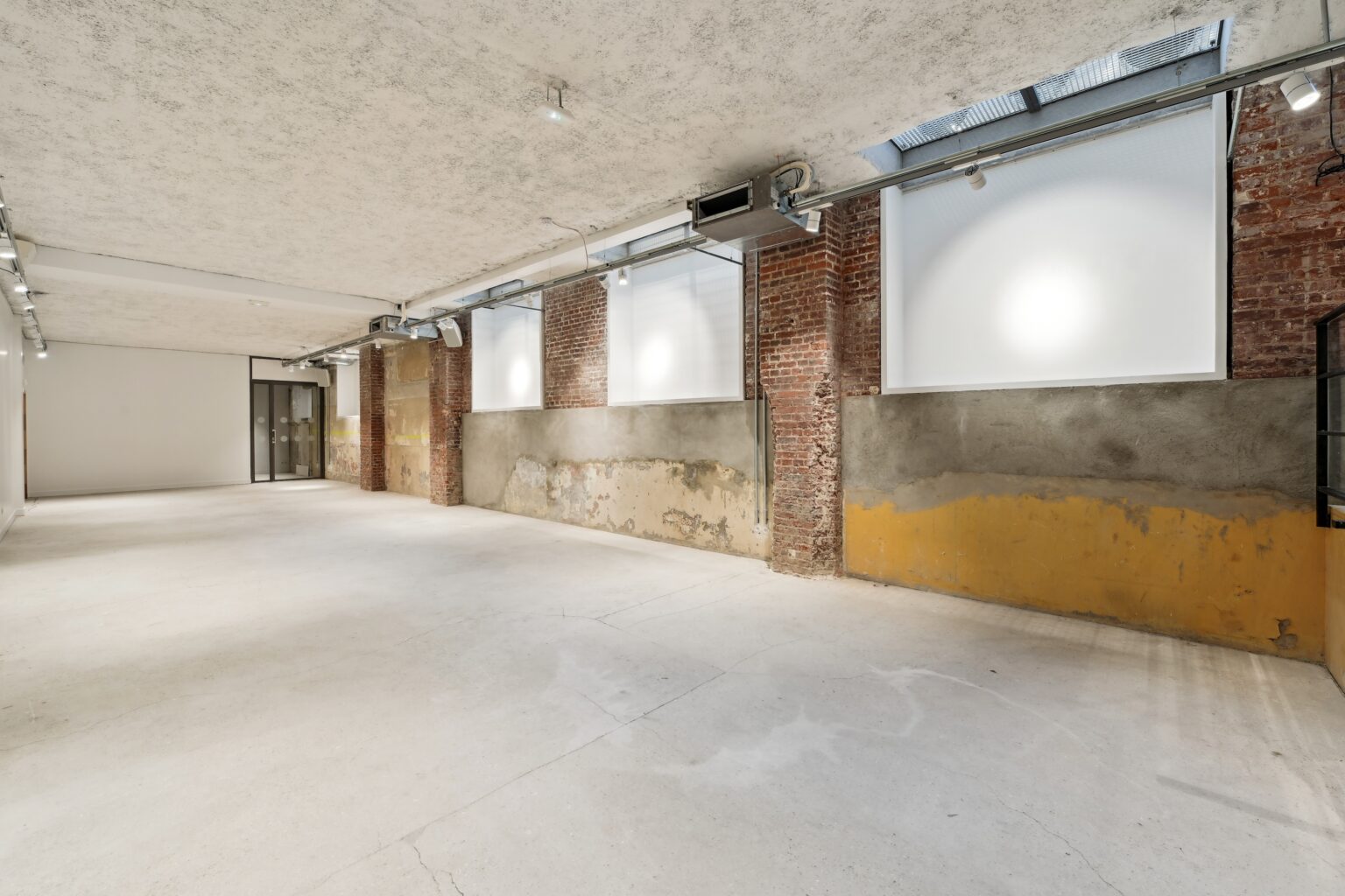 Wide interior view with brick piers, frosted windows, exposed surfaces, and a concrete floor.