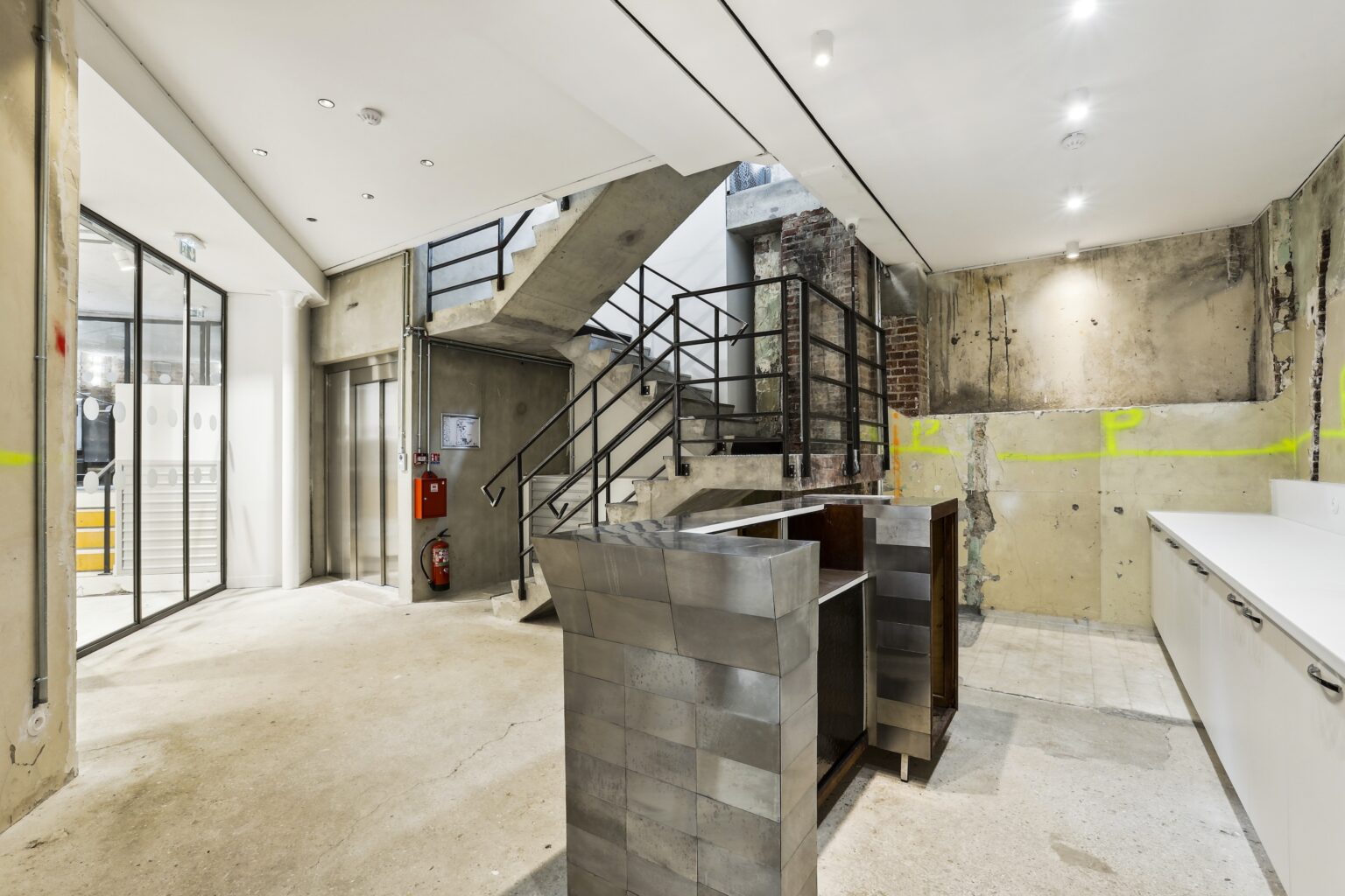 Lobby area with elevator and stairs, an industrial counter, and a kitchenette line along the wall.