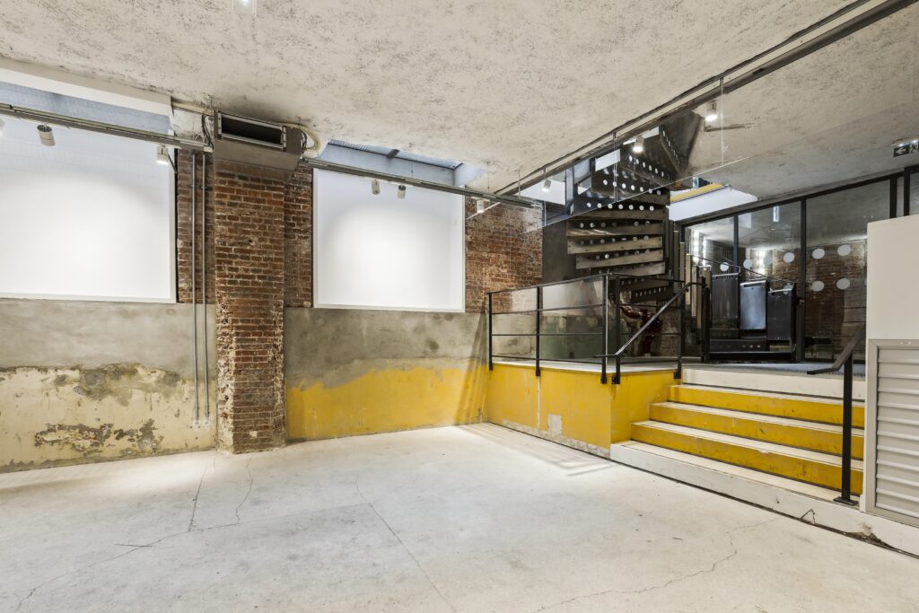 Split-level entrance with brick columns, yellow step platform, glass railing and spiral steel stair under a skylight.