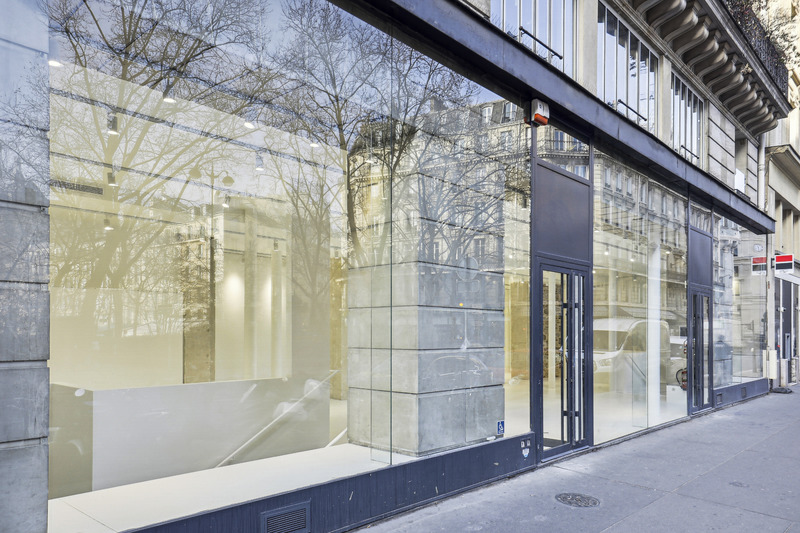 Side perspective of the showroom facade with continuous glazing and black framed entrance.
