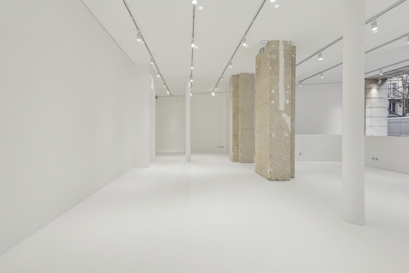 Wide interior view of a white showroom with track lights and raw stone columns.