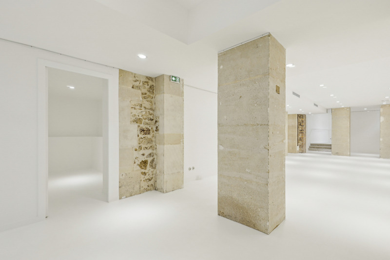 Interior view with a raw stone wall section, a large column, and an opening to an adjacent room.