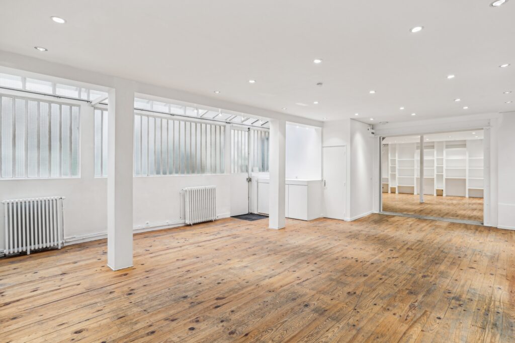 Ground floor showroom with white walls, wooden flooring and large windows.