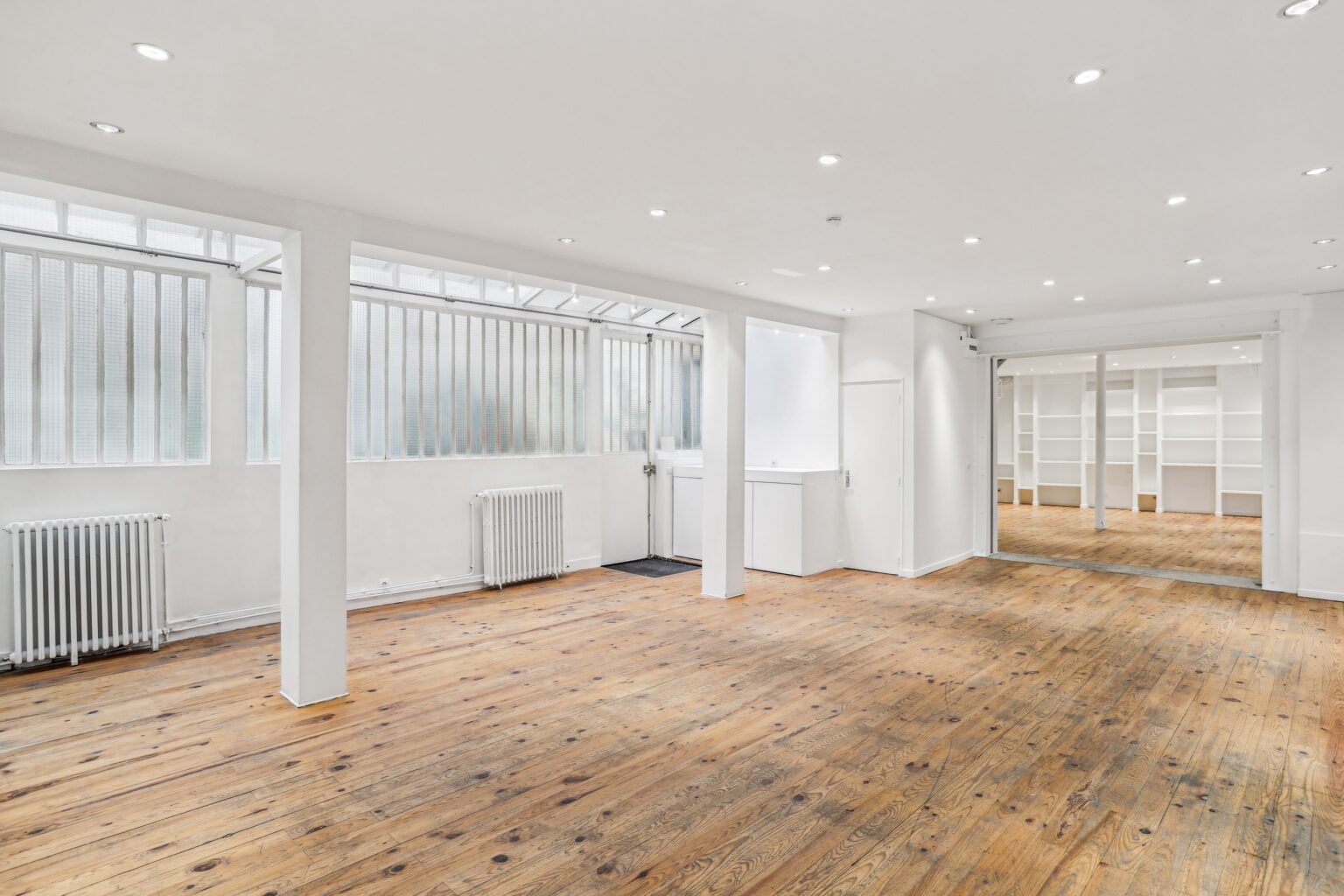 Ground floor showroom with white walls, wooden flooring and large windows.