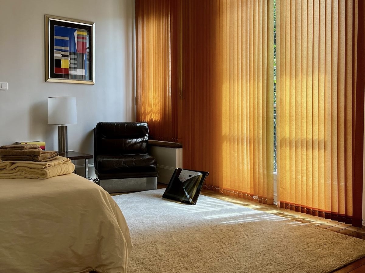 Bedroom at Villa Paul Strauss with warm curtains, wood flooring and lounge chair by the window.