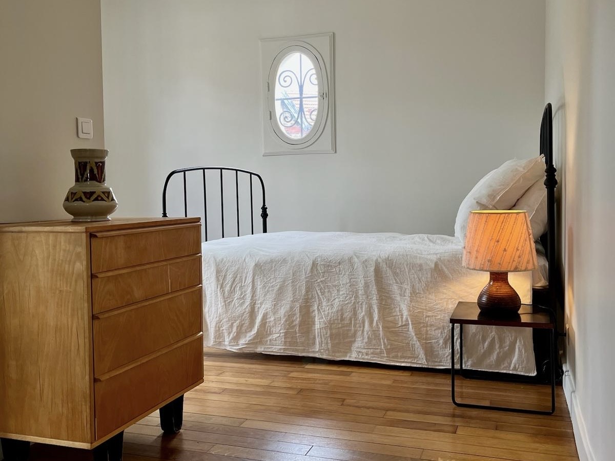 Quiet bedroom with dresser, bedside lamp and soft natural light.