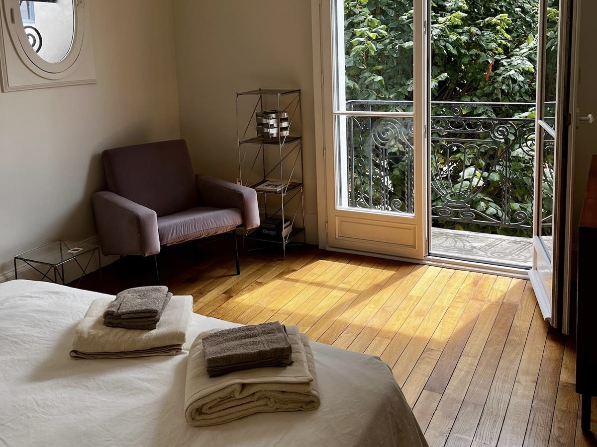 Bedroom at Villa Paul Strauss with terrace doors, armchair, wood flooring and folded towels on the bed.