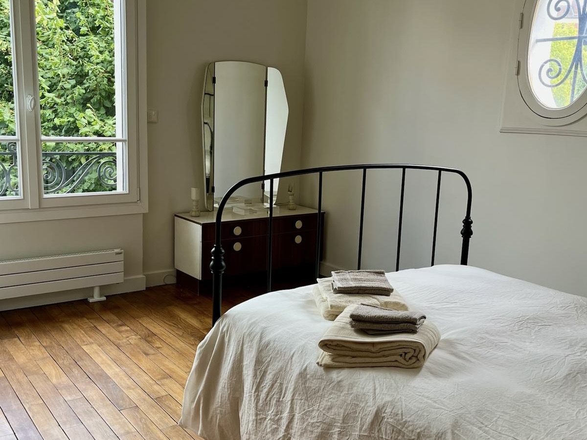 Bedroom at Villa Paul Strauss with iron bed frame, tall window and wood parquet floor.