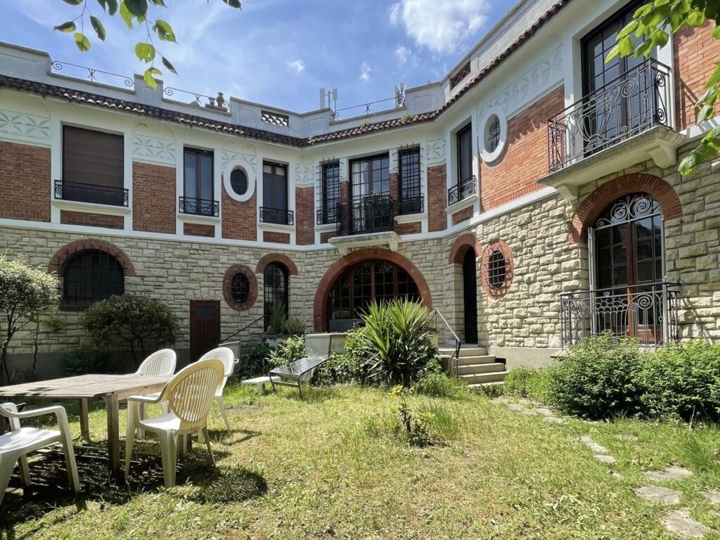 Courtyard at Villa Paul Strauss with brick facade, lawn, outdoor seating and landscaped greenery.