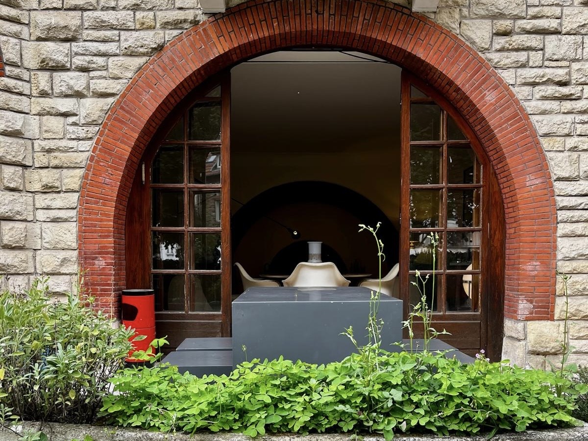 Arched entrance at Villa Paul Strauss with brick surround, glass doors and planted foreground.