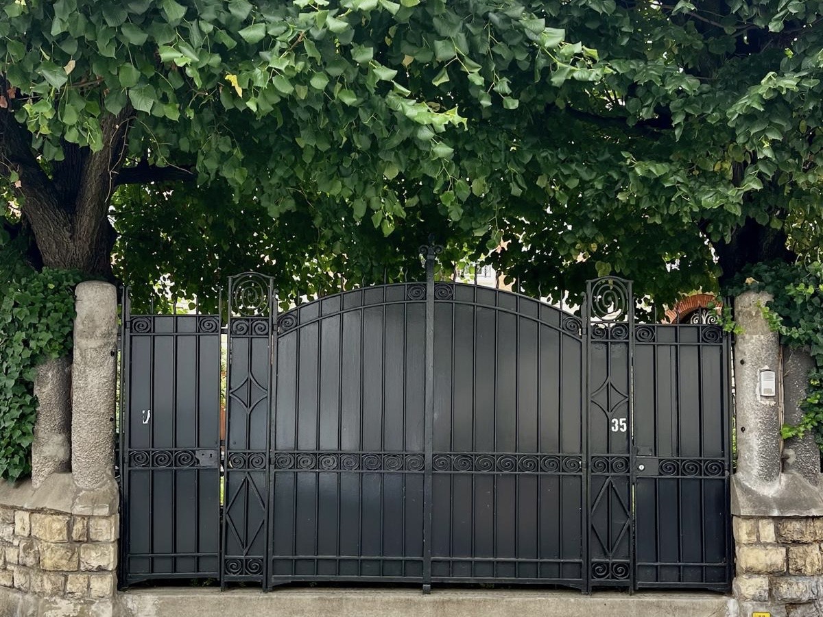 Exterior gate at Villa Paul Strauss framed by stone pillars and dense greenery.