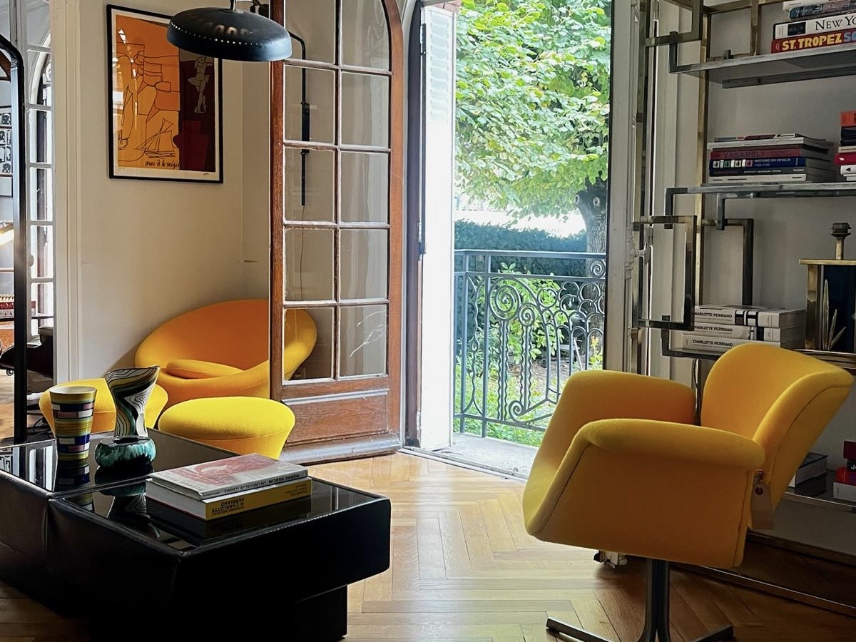 Lounge corner at Villa Paul Strauss with yellow chairs, side table and open window toward greenery.
