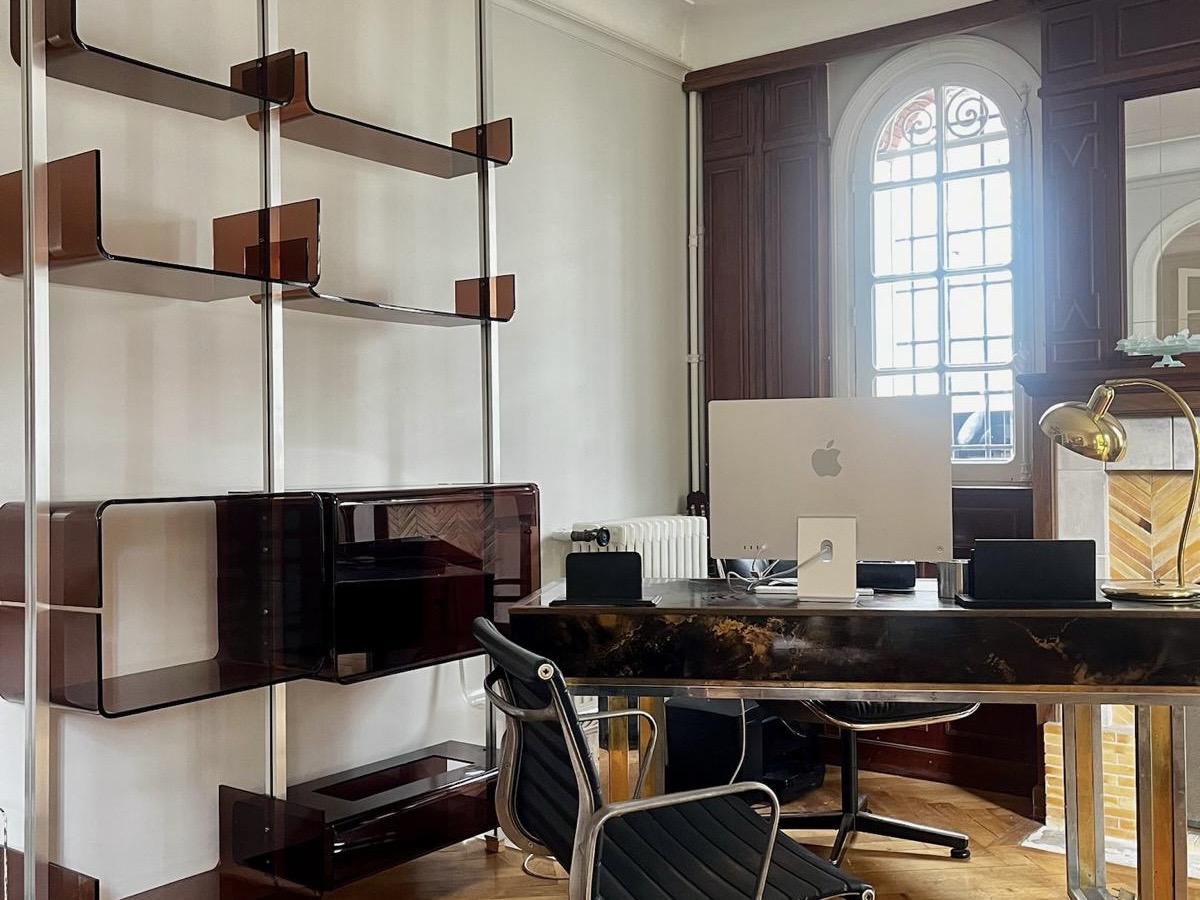 Office space with shelving, desk and tall arched window.