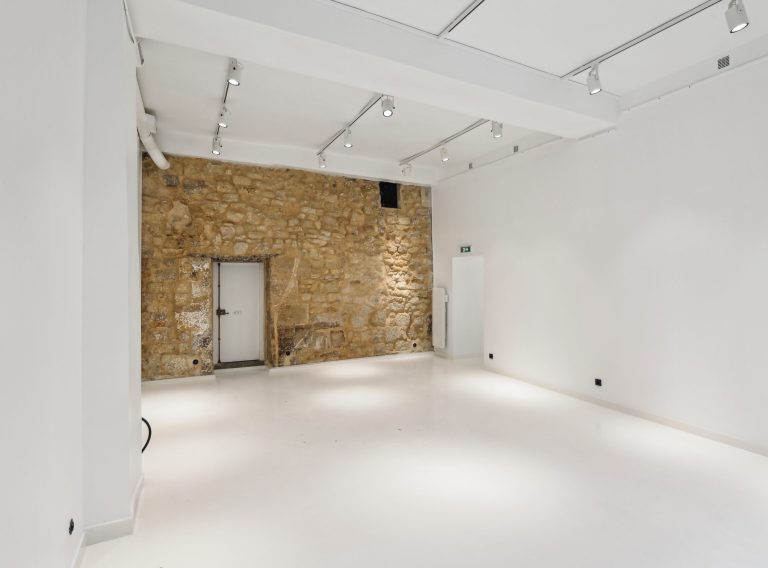 Angled view of stone wall with gallery track lighting — 52 Rue Charlot showroom
