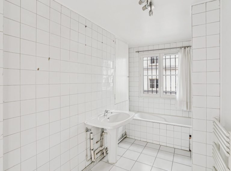 White tiled bathroom with window and tub in Paris showroom loft