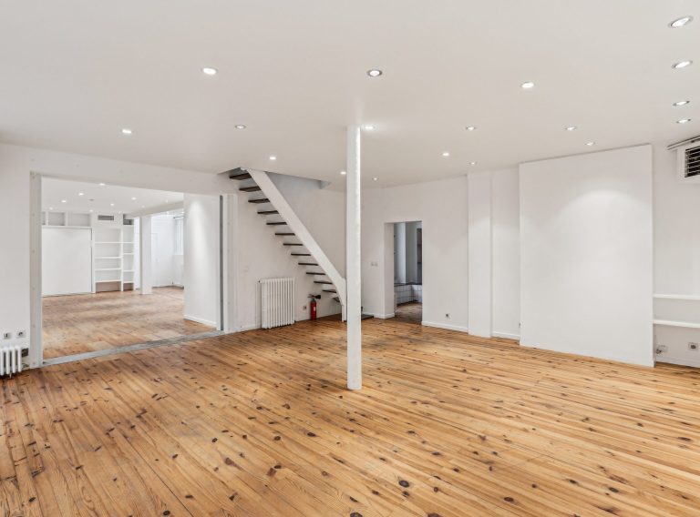 Open room with white stair and timber floor, ground-floor showroom Paris