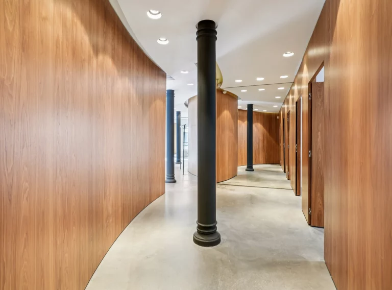 Corridor framed by wood walls with a central cast-iron column and ceiling spots.