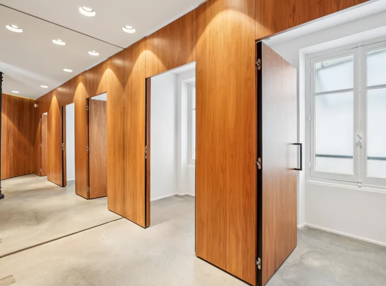 Adjustable wood partitions with open doors leading to a white side room.